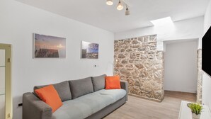 A modern living room with a grey sofa, orange cushions, a stone accent wall, and artwork on the wall.