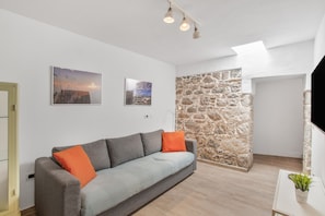 Una sala de estar moderna con un sofá gris, cojines naranjas, una pared de acento de piedra y obras de arte en la pared.