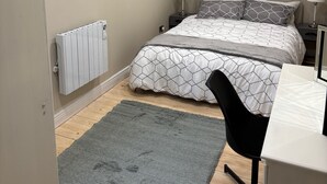 Un dormitorio con cama, lámparas de noche, escritorio, silla, radiador y luz de techo.
