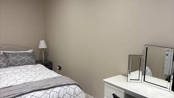 A bedroom with a bed, bedside table, lamp, dresser, chair, and mirror.