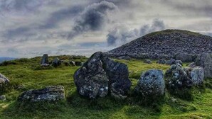 Un campo cubierto de hierba con grandes rocas y una colina al fondo.