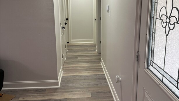 Un pasillo con piso de madera, paredes blancas y una puerta con un panel de vidrio decorativo.