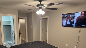 Un dormitorio con cama, ventilador de techo y televisor montado en la pared.
