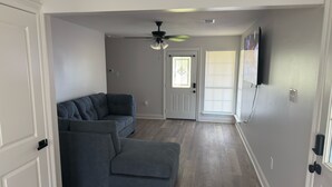 Una sala de estar con un sofá modular, un ventilador de techo y una puerta que da a otra habitación.