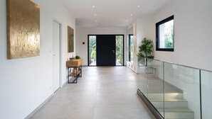 A modern hallway with a glass railing, a wooden bench, and a door leading to an outdoor area. - Villa Saint Aygulf - Vue mer avec Piscine Privée (Saint-Aygulf)