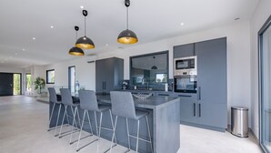 A modern kitchen with grey cabinets, a central island with bar stools, and pendant lighting. - Villa Saint Aygulf - Vue mer avec Piscine Privée (Saint-Aygulf)