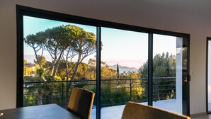 A modern room with a large sliding glass door leading to a balcony with a scenic view of trees and a distant landscape. - Villa Saint Aygulf - Vue mer avec Piscine Privée (Saint-Aygulf)