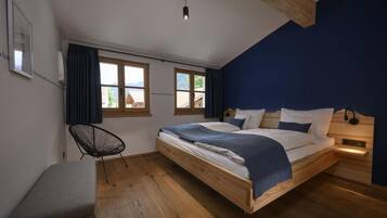 Ein Schlafzimmer mit einem hölzernen Bett, einem Sessel, einer Bank und einem Fenster mit Vorhängen.