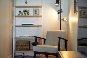A room with a chair, shelves with books and decorative items, a floor lamp, and a woven basket.