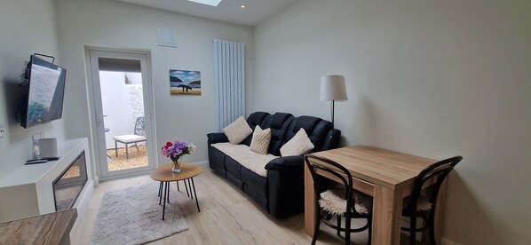 Una sala de estar moderna con un sofá, una mesa de madera, un televisor y una mesita auxiliar con flores.