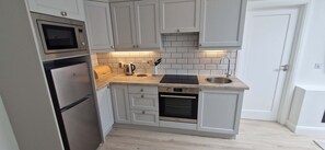 A compact kitchen with white cabinetry, a built-in oven, a microwave, a sink, and a toaster.