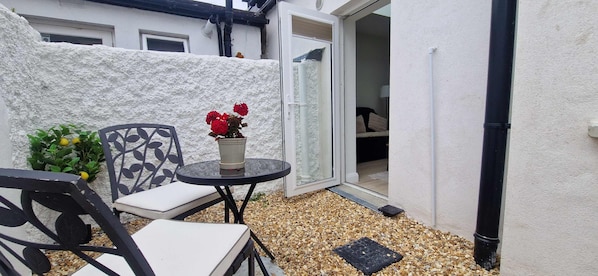 A small patio with a table and chairs, a potted plant, and a white wall.