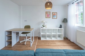 A modern room with a wooden floor, a white desk with a chair, a white shelving unit, a floor lamp, and a window with curtains. - Quirky 1BD Flat, Heart of Sydenham (Greater London)