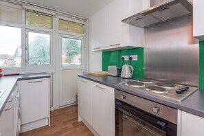 A modern kitchen with white cabinets, a stainless steel range hood, a gas stove, and a green backsplash.