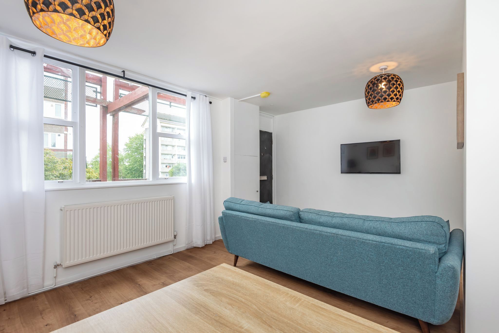 A modern living room with a sofa, a radiator, a TV, and a window with a view of buildings.