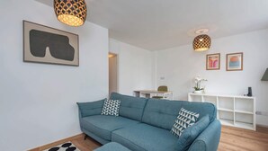 A living room with a sofa, ottoman, patterned rug, and artwork on the wall.