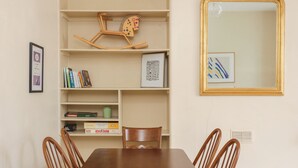 Een eetgedeelte met een houten tafel en stoelen, een boekenkast met boeken en een schommelpaard, en een inlijstte spiegel aan de muur.