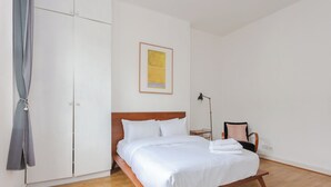 Een verzorgde slaapkamer met een houten bed, witte beddengoed, een lijstwerk aan de muur, een nachtkastje met een lamp en een stoel.