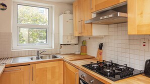 Een keuken met houten kastjes, een gasfornuis, een spoelbak en een raam met uitzicht op groen.