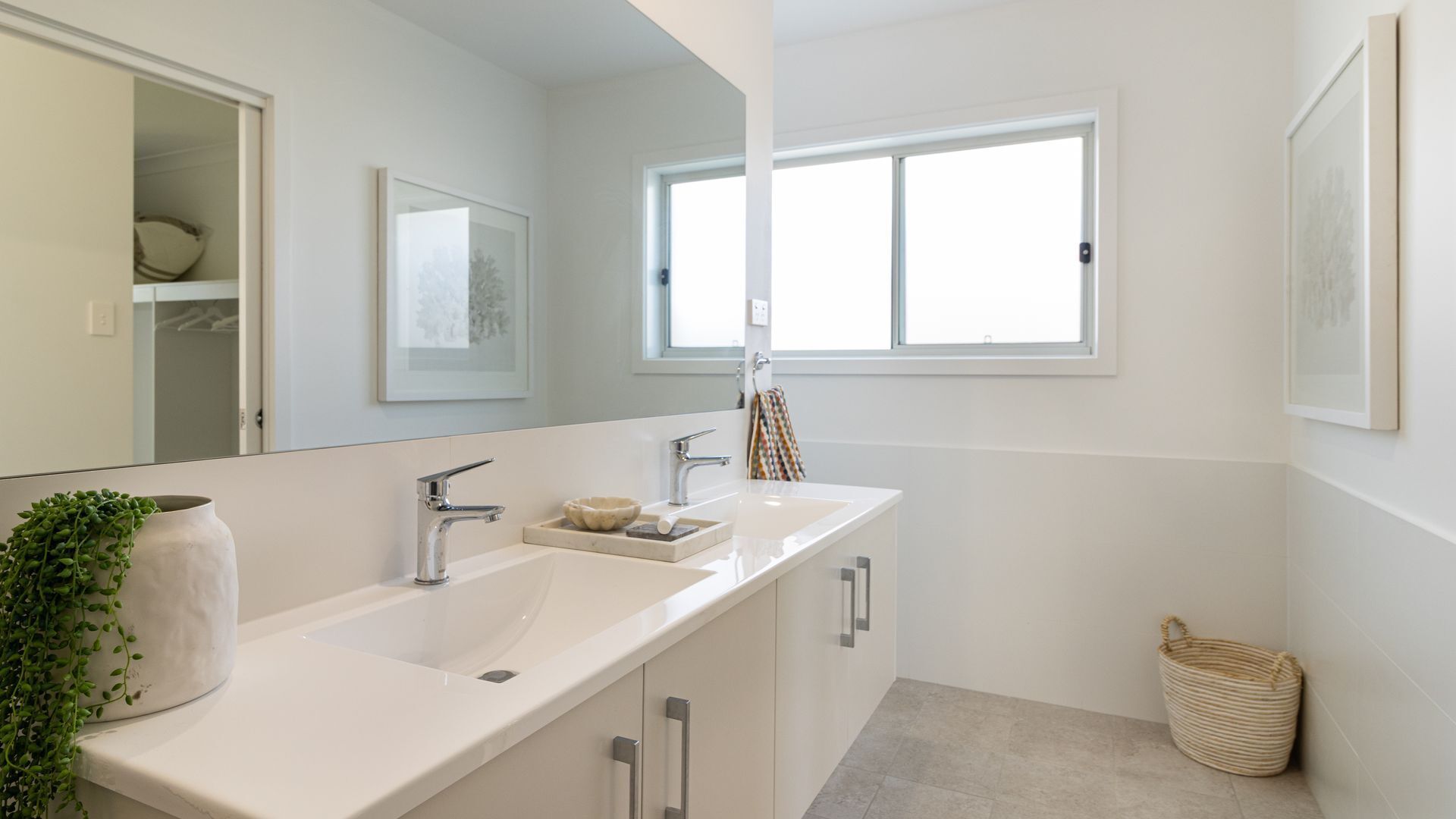 Un baño moderno con un espejo grande, dos lavamanos, una ventana y una planta.