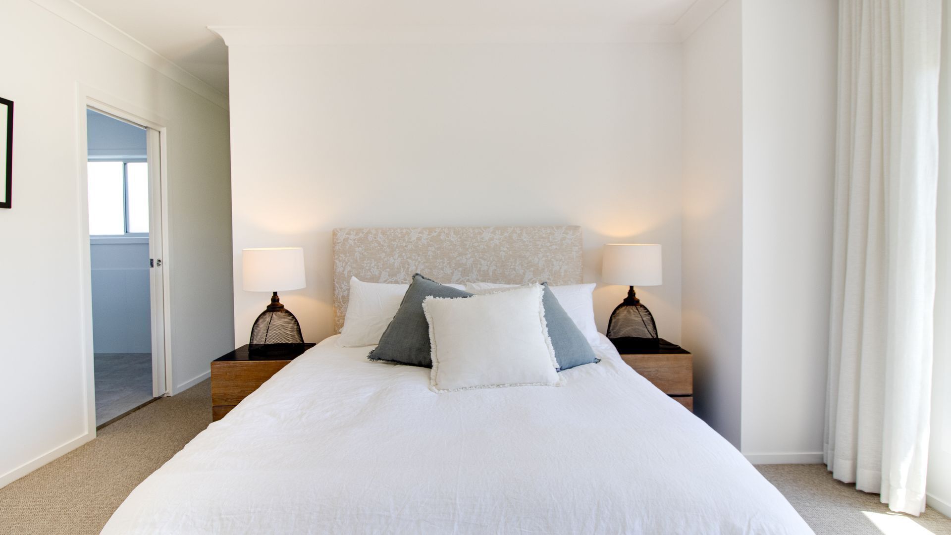 A hotel room with a large bed, two bedside tables with lamps, a headboard with a floral pattern, and a door leading to another room.