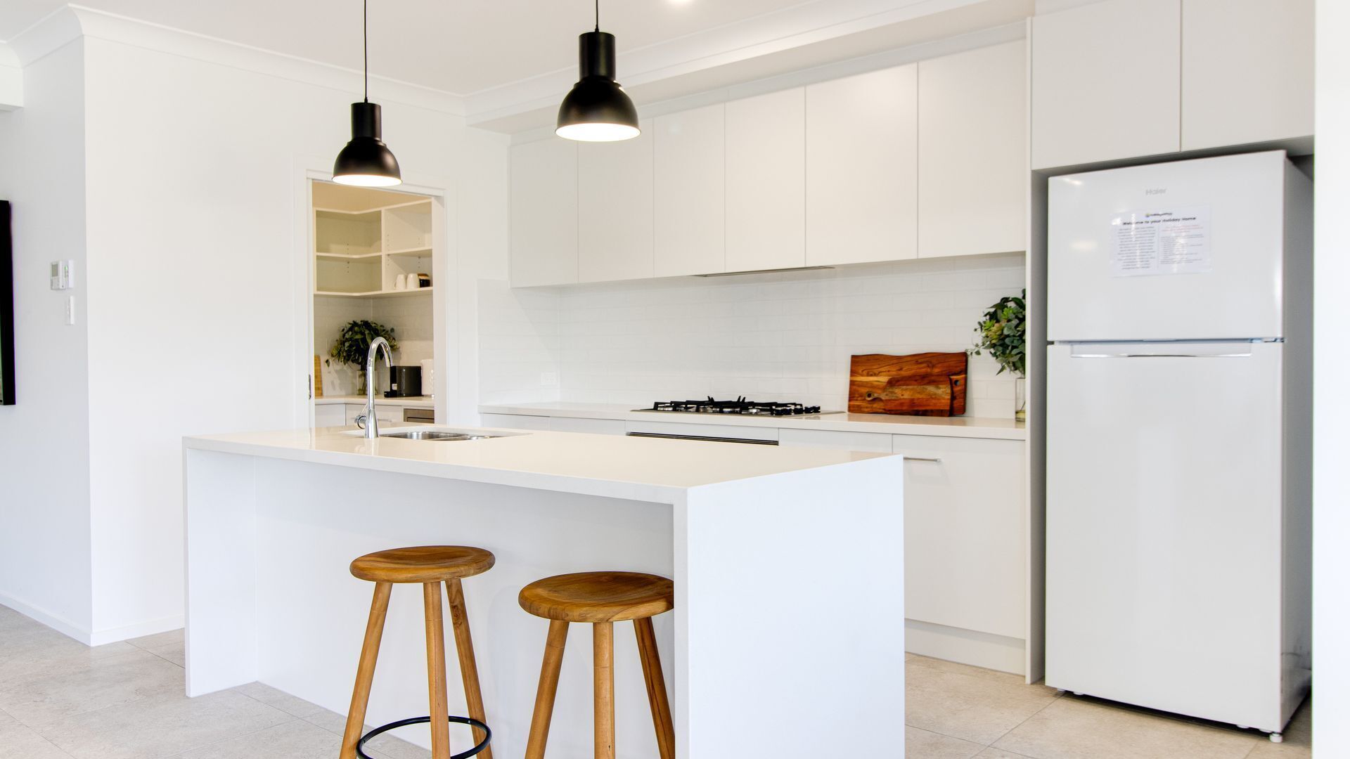 Eine moderne Küche mit weißen Schränken, einer zentralen Kochinsel mit Sitzgelegenheiten, einem Gasherd und einem Kühlschrank.