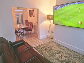 Un salon doté d’un téléviseur à écran plat fixé au mur, d’un canapé en cuir marron, d’un tapis à motifs et d’un coin repas avec une table et des chaises.