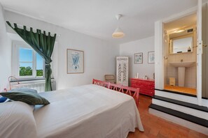 Une chambre à coucher comprenant un lit, un bureau, une chaise, une armoire et une salle de bain visible à travers une porte ouverte.