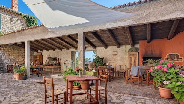 Un patio al aire libre rústico con suelo de piedra, mobiliario de madera y plantas en macetas.