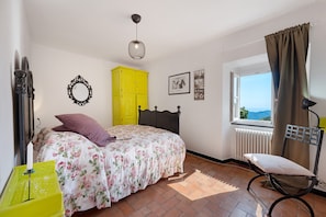 A bedroom with a bed, a yellow wardrobe, a window with a view, a mirror, and a lamp.