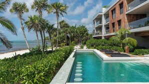 Um hotel moderno com piscina, palmeiras e vista para o oceano.