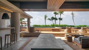 An outdoor lounge area with a long table, seating, and a view of the ocean. - Beachfront Luxury + Rooftop Oasis Tankah Bay (Tulum)