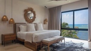 A bedroom with a large bed, bedside tables, a bench, a mirror, and a view of the ocean. - Beachfront Luxury + Rooftop Oasis Tankah Bay (Tulum)