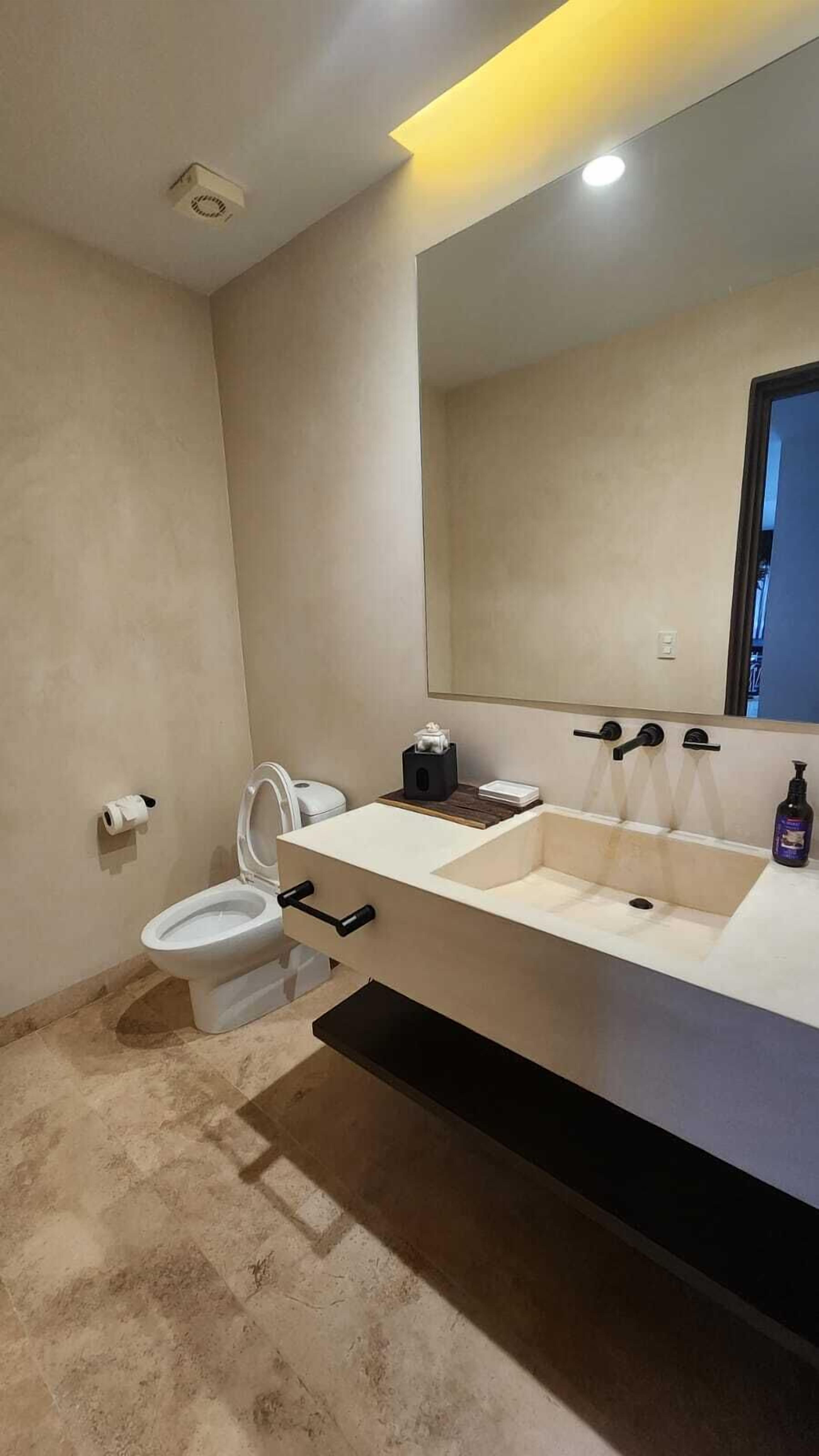Ein modernes Badezimmer mit einem weißen Waschbecken, einer Toilette und einem großen Spiegel.
