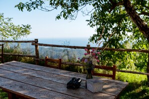 Una mesa de madera con unos binoculares y un recipiente metálico, un jarrón con flores y una valla de madera con vistas al paisaje.