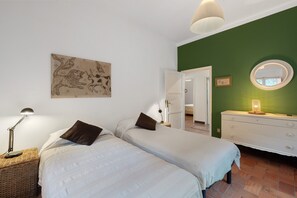 Un dormitorio con dos camas, una mesita de noche con lámpara, un aparador, un espejo y una pared de acento verde.
