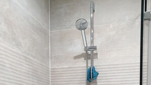 Eine Dusche mit Duschbrause, Wandarmatur und Reinigungsbürste. Auf dem Boden stehen eine Flasche Flüssigseife und eine Lotionflasche.