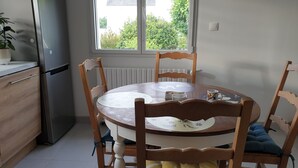 Eine Küche mit einem runden Holztisch, Stühlen, einem Kühlschrank und einem Fenster mit Blick auf Grünflächen.