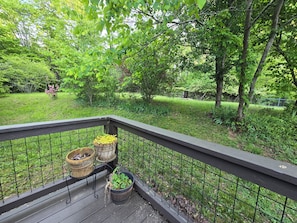 A wooden deck with a metal railing, potted plants, and a view of a lush green garden.