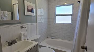 Une salle de bain avec un lavabo, des toilettes, une baignoire et une fenêtre.