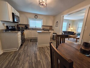 A modern kitchen with white cabinets, a microwave, and a dining area with a wooden table and chairs. - Charming Mountain Retreat with fire pit, fenced yard, scenic views, and privacy. (Mineral Bluff)