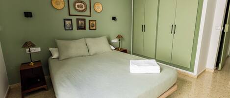 A bedroom with a bed, green wardrobe, framed pictures, and two bedside tables with lamps.