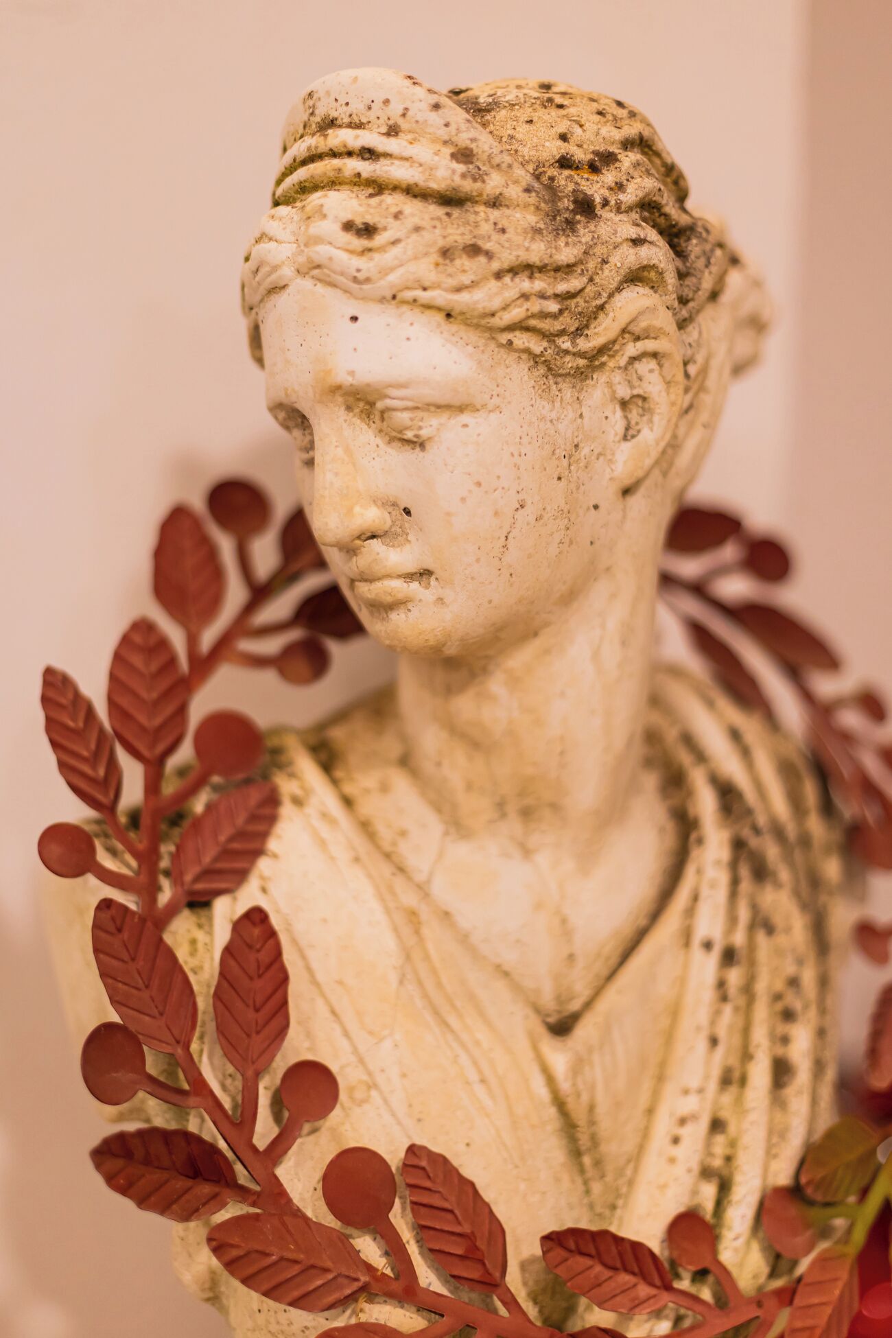 Une sculpture en marbre représentant un buste, avec un vêtement drapé et des feuilles rouges.