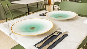 A dining table with two plates and cutlery, green chairs, and a marble table surface. - HN Salteras (Salteras)