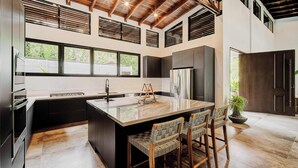 A modern kitchen with a large island, built-in appliances, and a high ceiling with exposed beams.