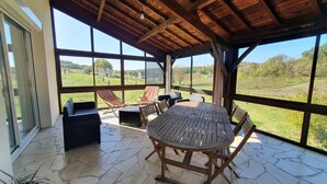 Un espace extérieur abrité, doté d’un sol en pierre, de meubles en bois et de grandes fenêtres offrant une vue sur la campagne.