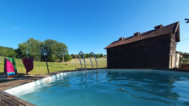 Une piscine avec une terrasse en bois, un escalier en métal et un bâtiment en bois en arrière-plan.