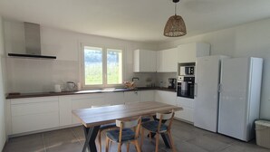Une cuisine moderne avec des meubles blancs, une table en bois, deux chaises, un luminaire suspendu et un réfrigérateur.
