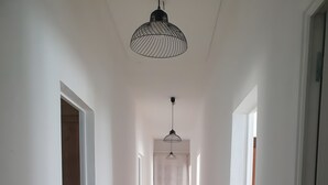 Un couloir aux murs blancs, au sol en bois et doté d’un luminaire suspendu.