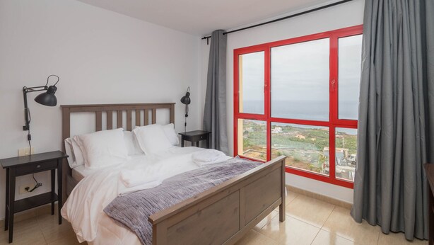 A bedroom with a bed, two bedside tables, a window with curtains, and a view of the outside. - 2BR BuenaVida Residential - Mountain Views 2ºD (Breña baja)